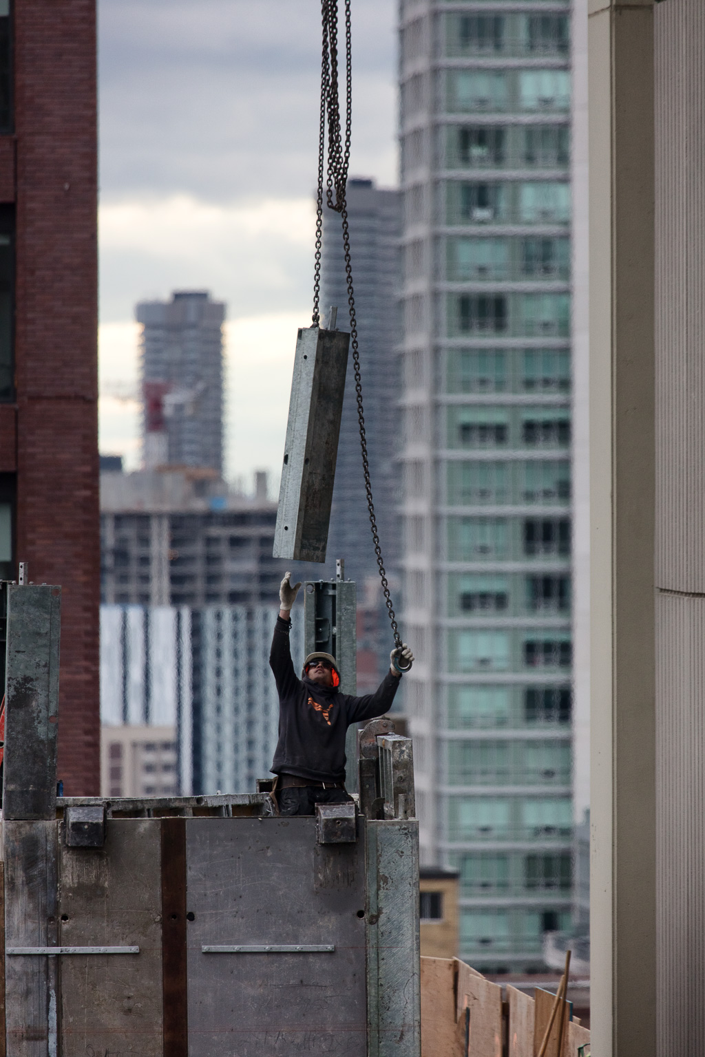 Construction worker reaches for piece of metal suspended by a chain