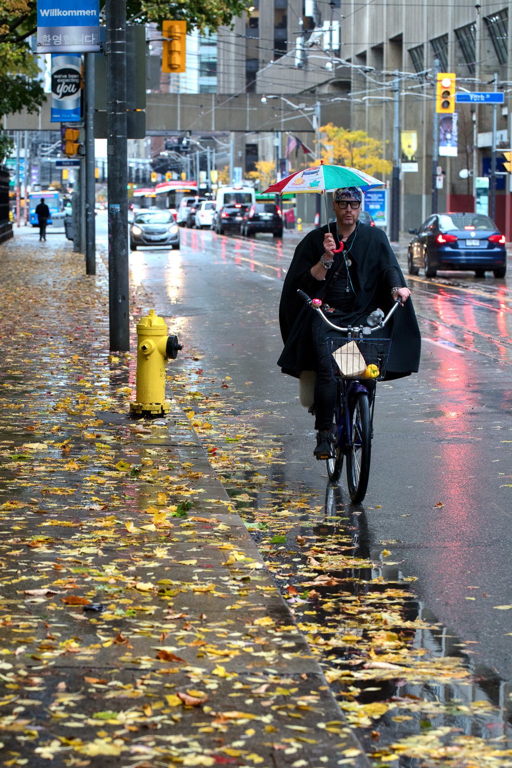 Person cycles down Queen Street West while holding an umbrella