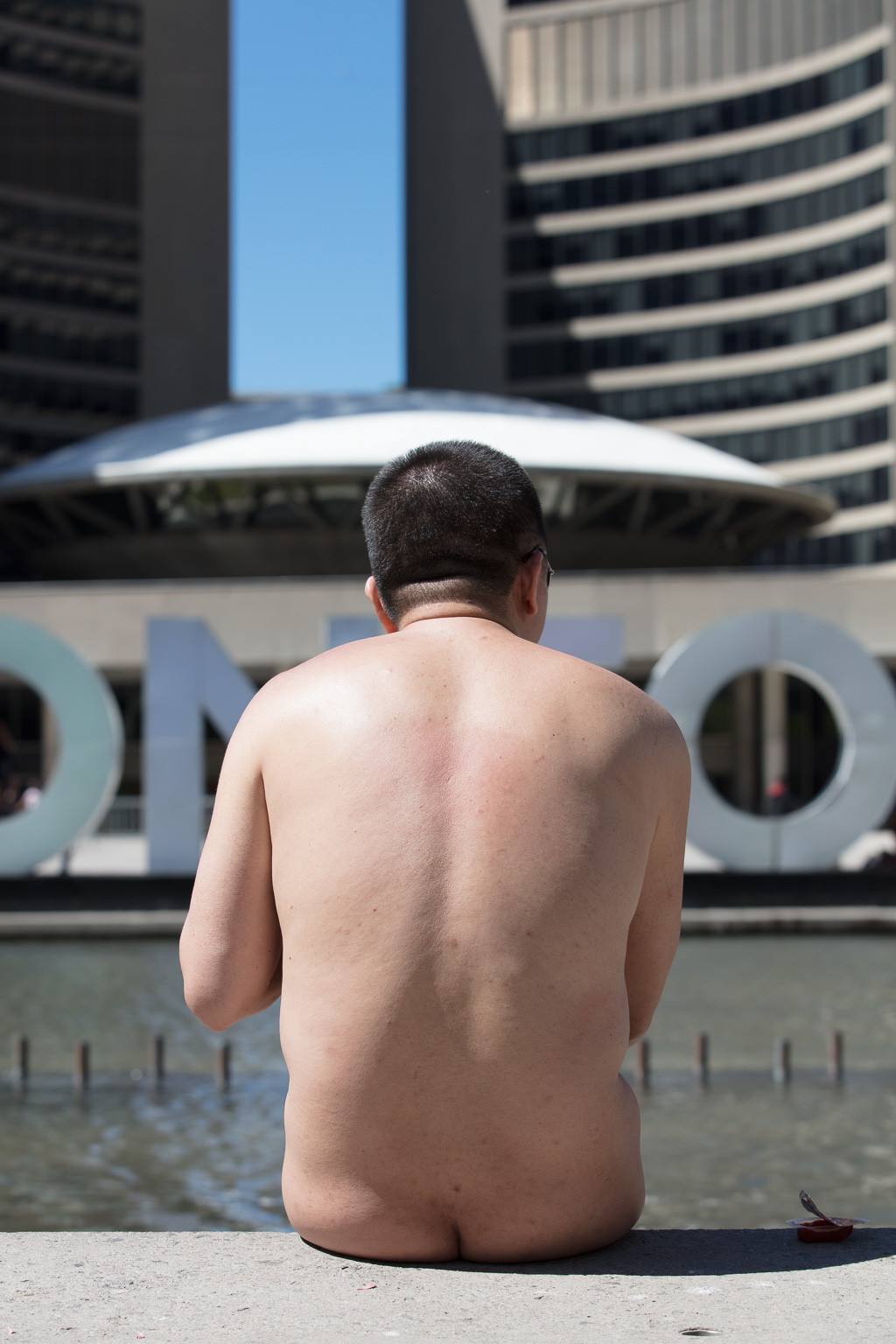 Naked man sits in front of Toronto's City Hall.