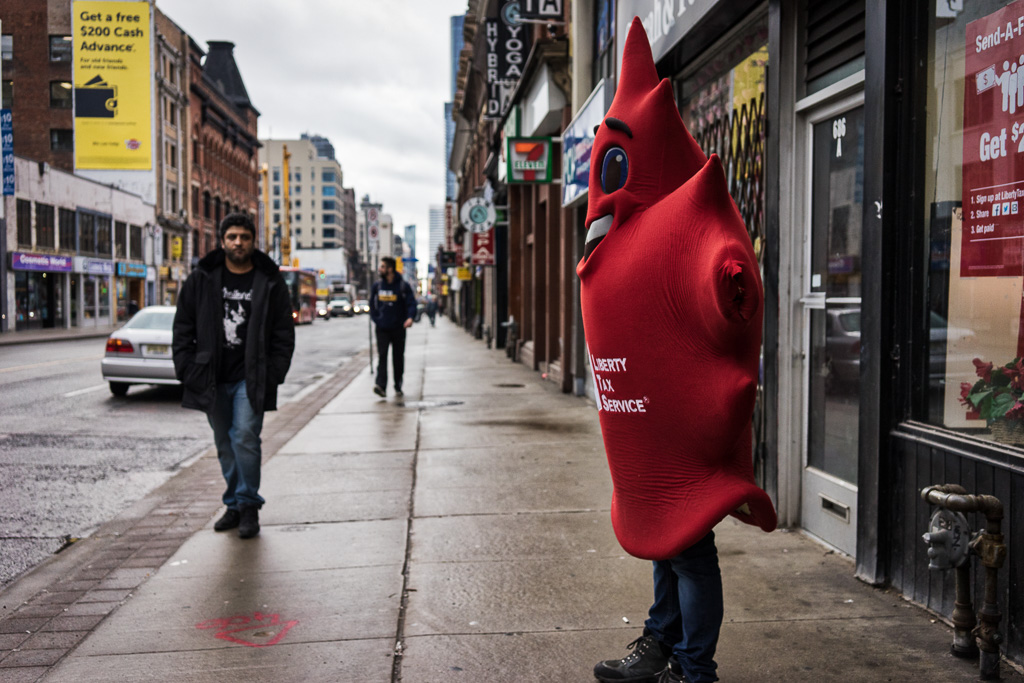 Person stands on sidewalk wearing a maple leaf suit to promote a tax preparation service
