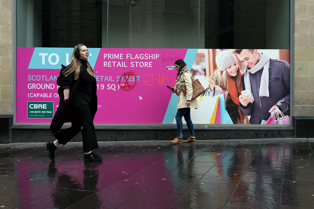 Woman walks past a sign advertising retail space for a flagship store.