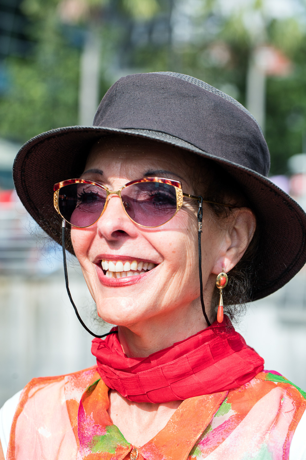 Smiling woman wearing hat and sunglasses with red scarf