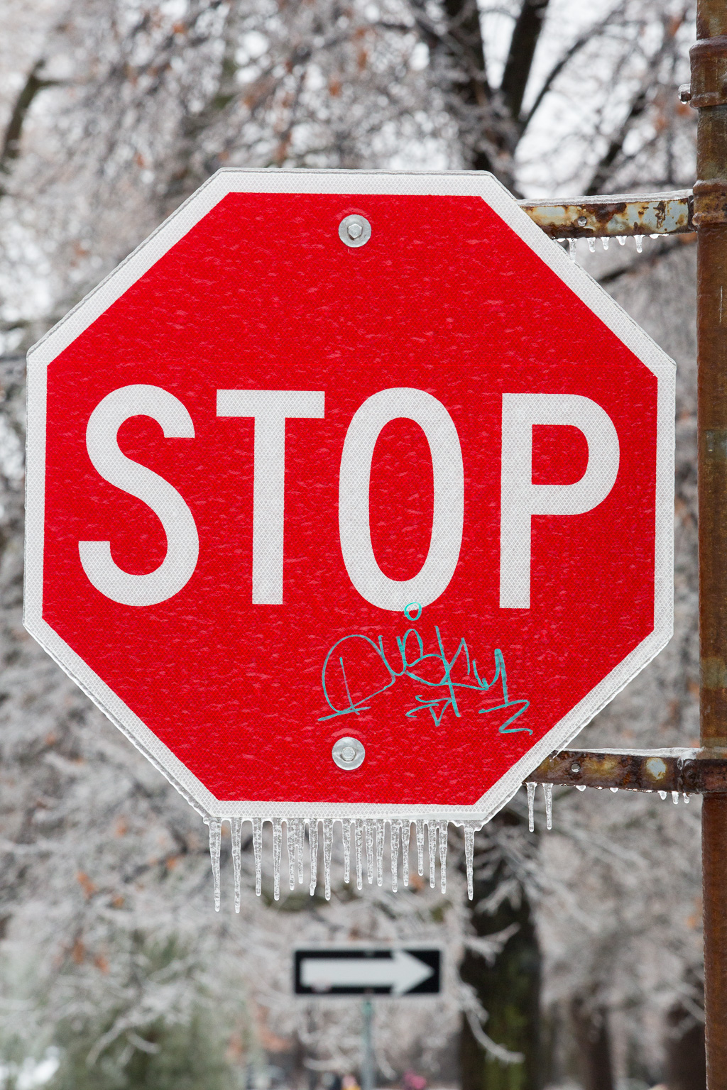 Stop sign in ice storm with icicles dangling from the bottom.