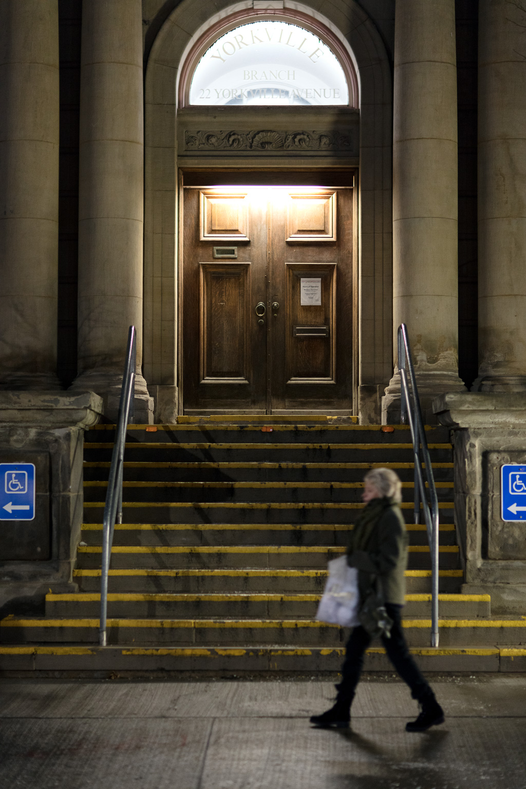 Night shot of a woman walking past the entrance to the Yorkville Public Library in Toronto