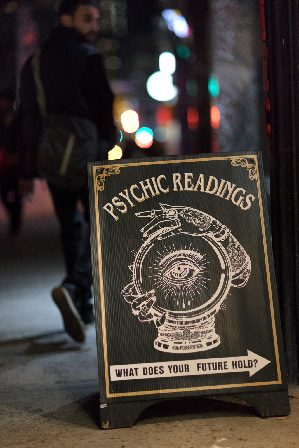 Man walking along sidewalk gazes back at sign advertising psychic readings.