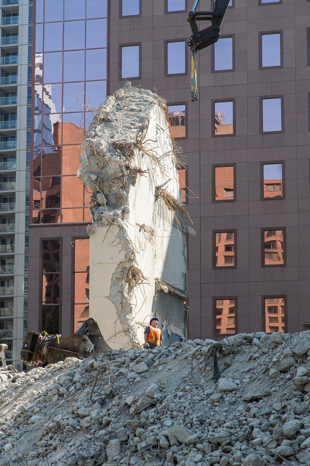 A tiny construction worker stands in front of a large upright slab of concrete as the last of a building is being demolished.