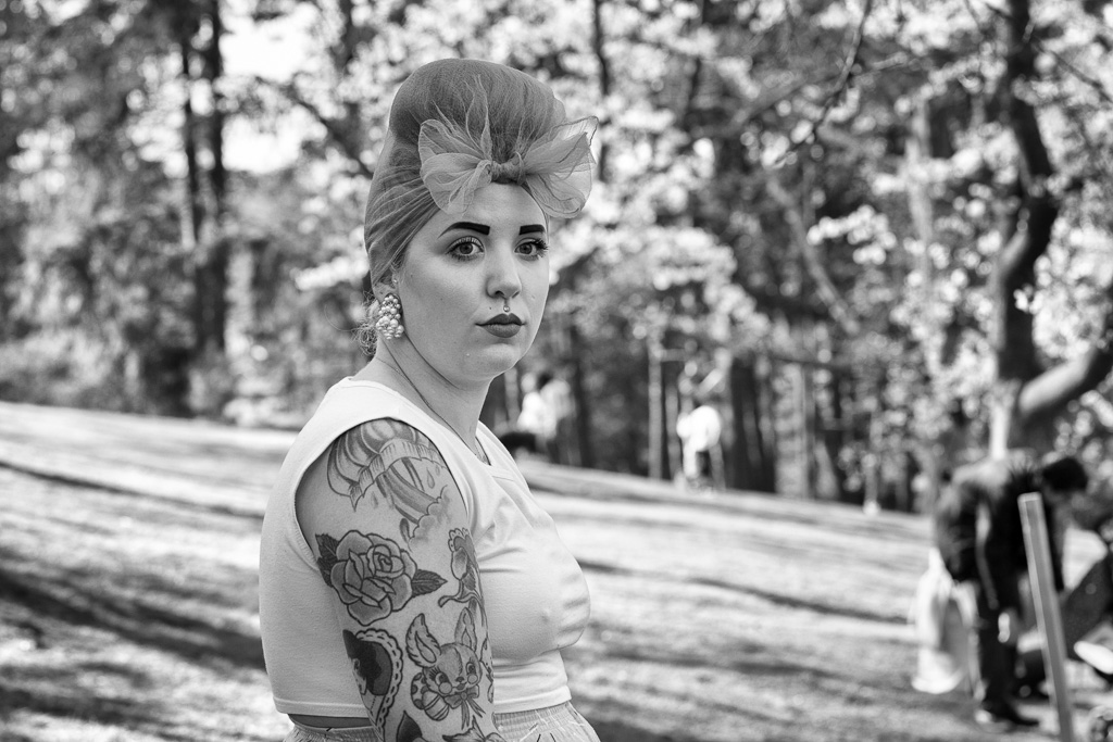A woman with a heavily tattooed arm, and wearing strong makeup and a hairnet, sits in Toronto's High Park.