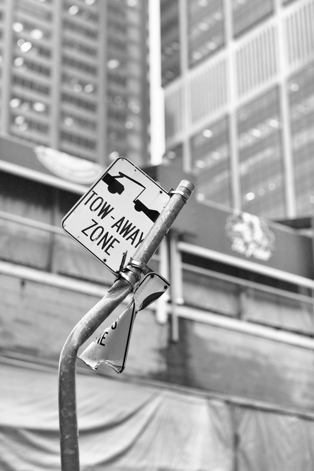 Tow-Away Zone sign on a bent metal pole with tall buildings in the background.
