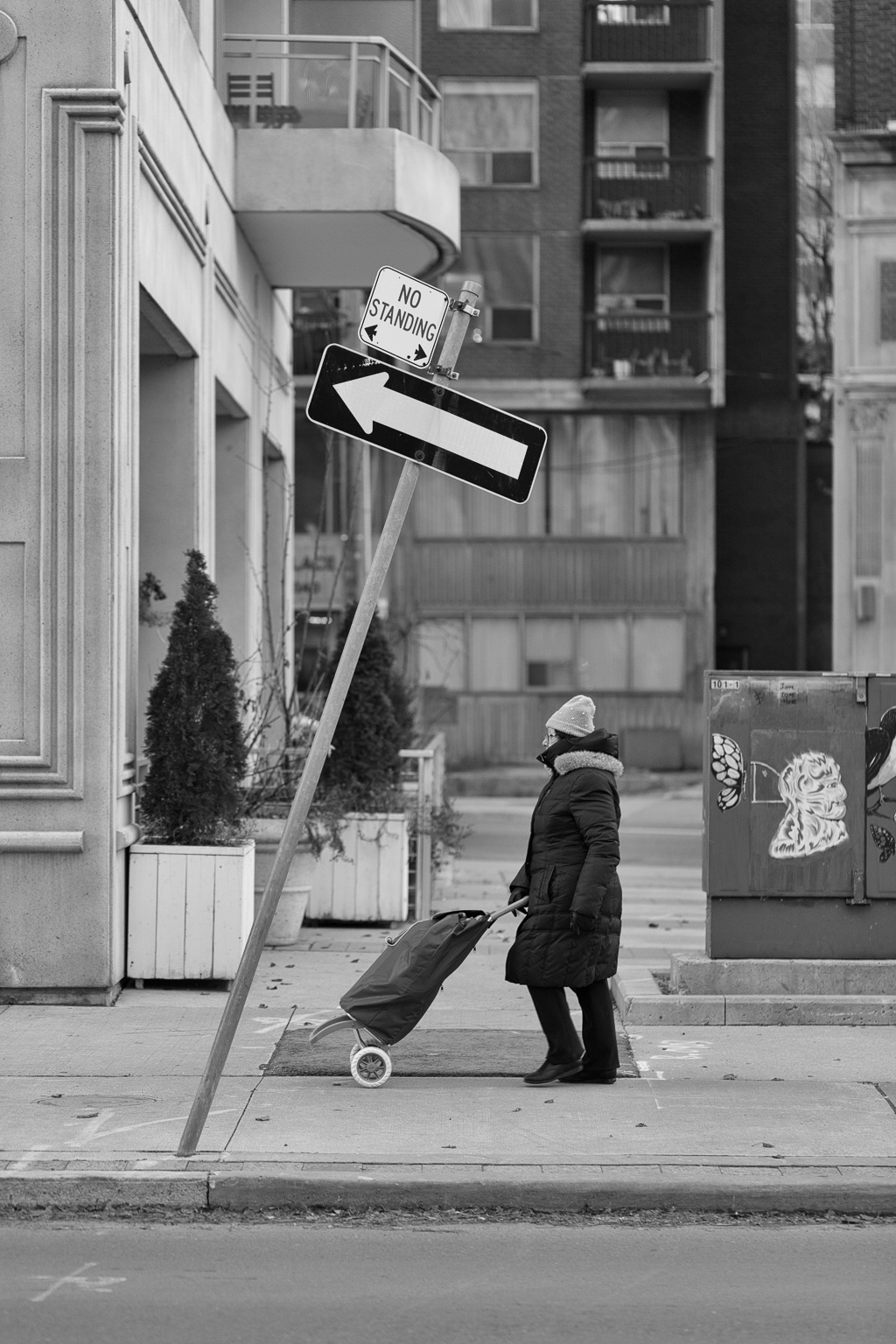 A woman pushes a bundle buggy along the sidewalk while, overhead, an arrow points off at an inclined angle.
