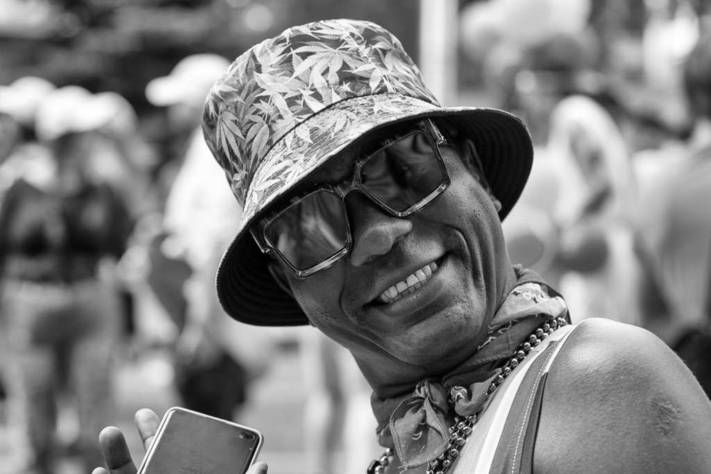 Street portrait of a man wearing sunglasses and a cannabis decorated fishing hat.