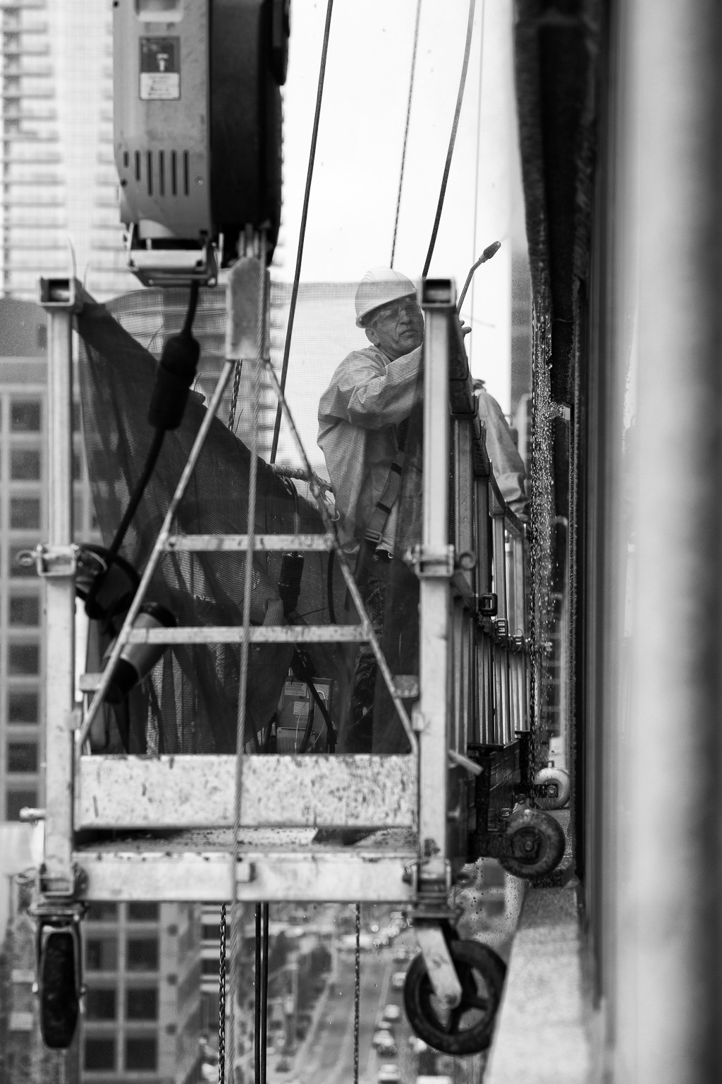 A worker stands on staging, power washing the side of a building high above Bloor Street, Toronto.