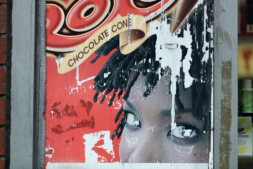 Worn advertisement with the words "Chocolate Cone" appearing on a ribbon above a portion of a face that excludes the mouth.