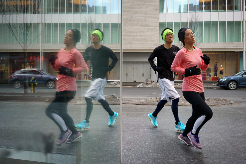 A young couple go for a morning run and their image is reflected in a store window as they round the corner.