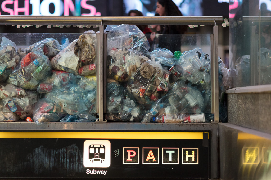 A night photograph of bags of consumer waste piled up by the Dundas Street entrance to Toronto's subway.