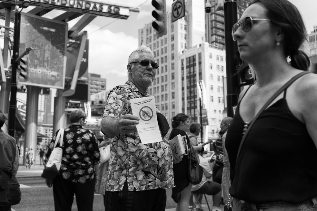 A man offers a pamphlet to a passer-by who ignores him completely.