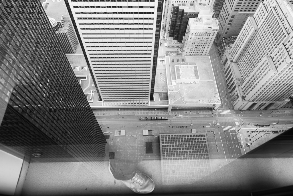 View from above staring down onto King Street West and Toronto's Financial District. A translucent image of the photographer's foot appears reflected in the window.