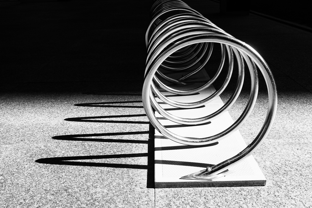 A bicycle rack casting a shadow in late afternoon sunlight and receding into a shaded distance.